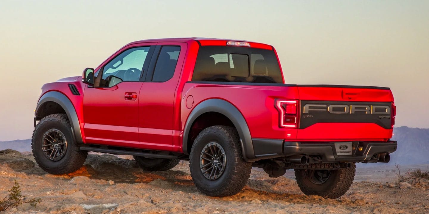A side shot of a Red Ford F-150 Raptor driving through the dessert.
