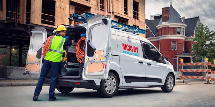A worker in a yellow vest loading supplies into the back of a Ford Transit Connect Cargo Van.
