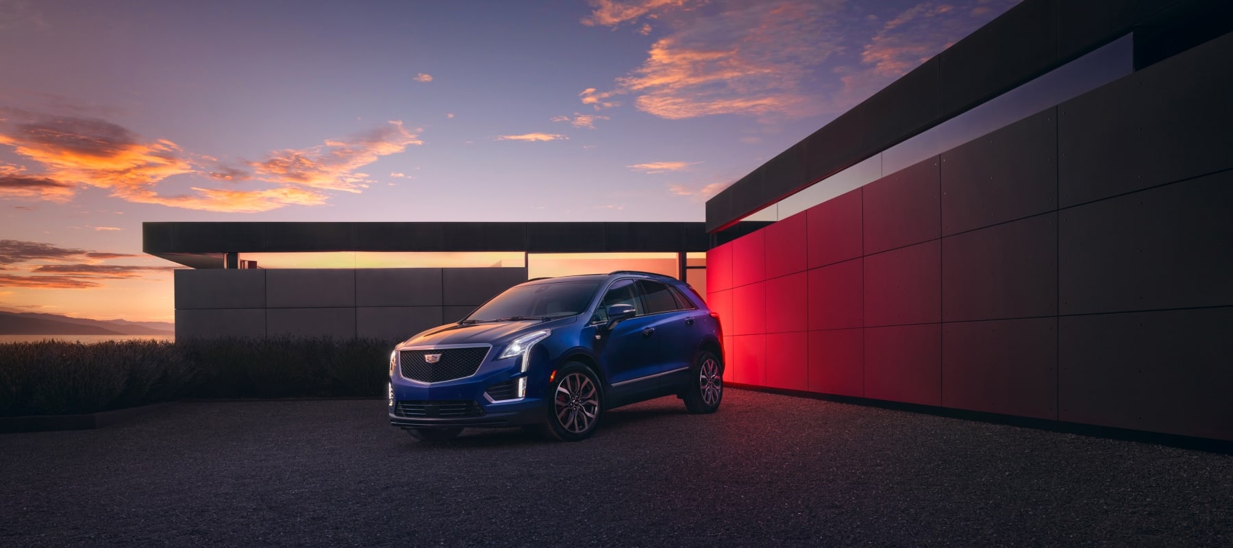 An exterior shot of a Cadillac SUV with dramatic sunset. 