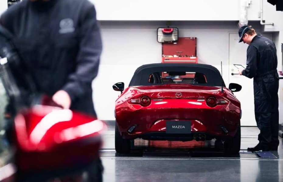 A service technician is working on a red Mazda