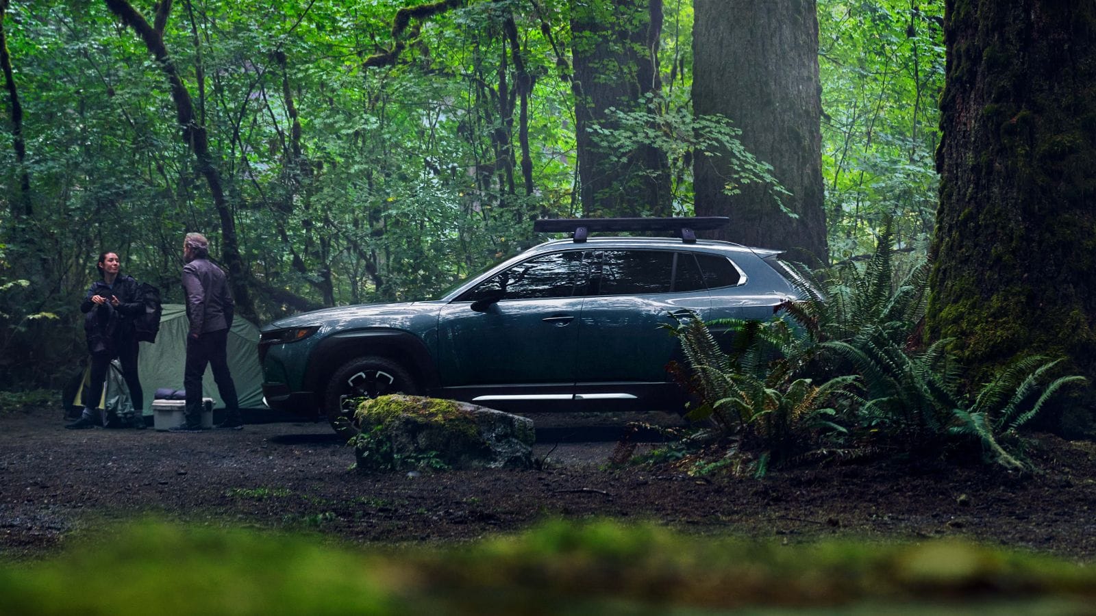 Side shot of CX-50 on forest road with owners moving their camping gear