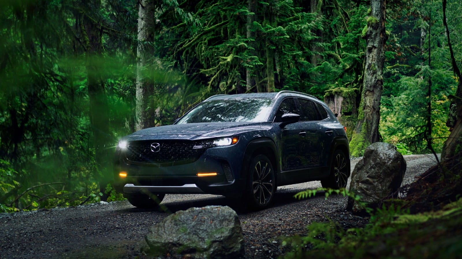 Front angled shot of CX-50 on forest road with daytime driving lights on