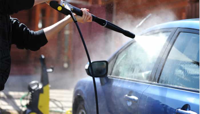 Persona con manguera rociando la ventanilla de un coche