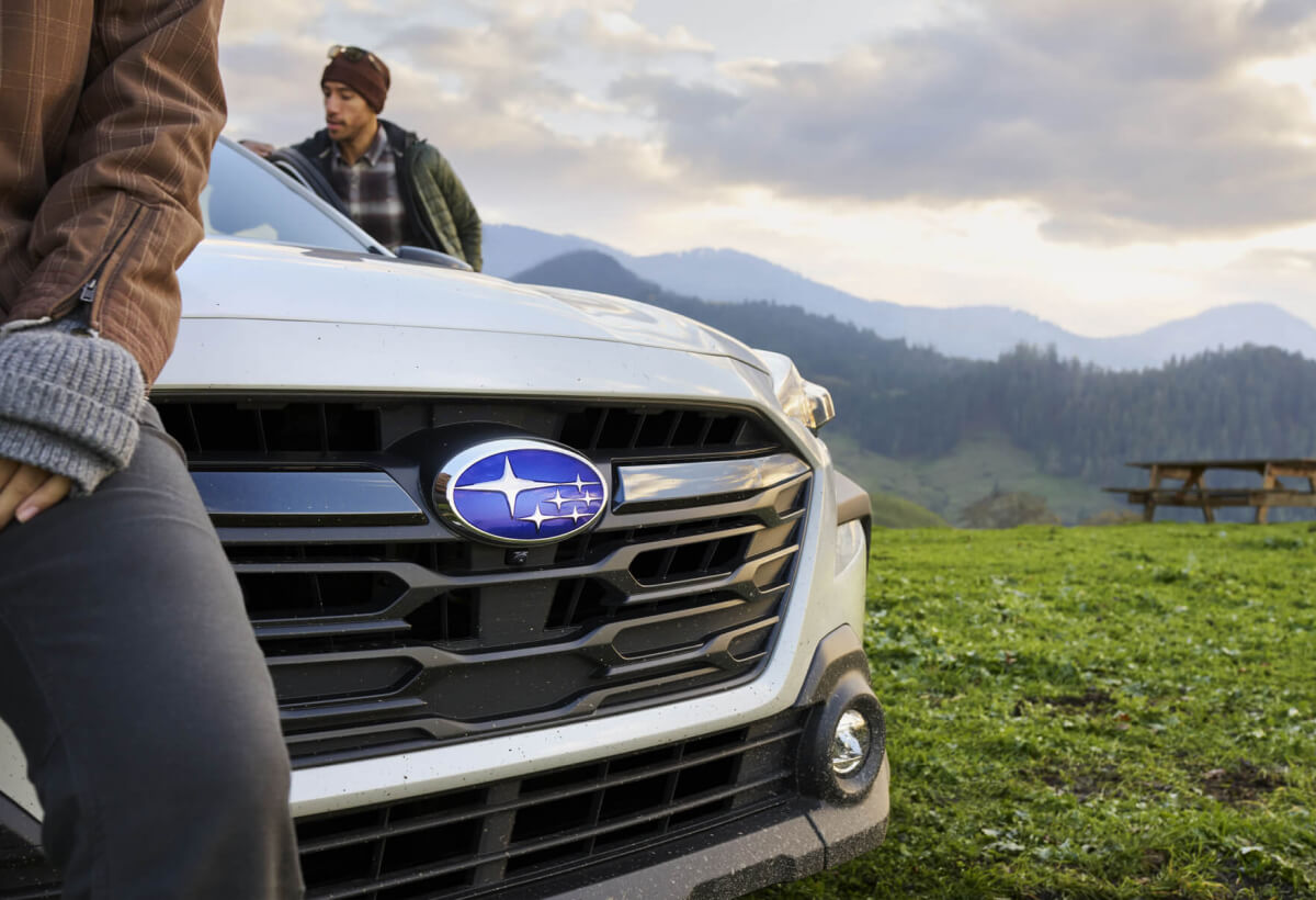 2023 Subaru vehicle front bumper and badge with someone sitting on the hood in a mountainous landscape